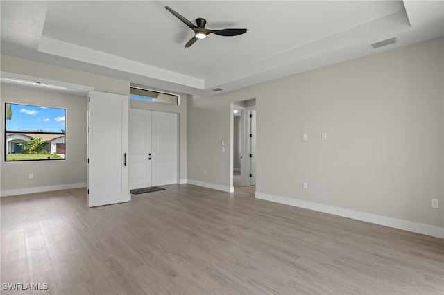 unfurnished bedroom with a tray ceiling, light wood-type flooring, and ceiling fan