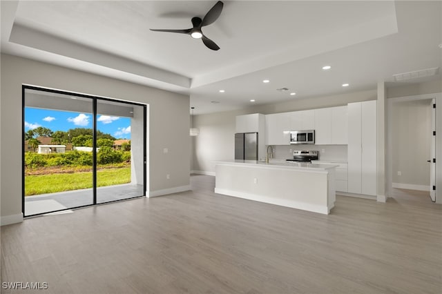 unfurnished living room with light wood-type flooring, a raised ceiling, sink, and ceiling fan