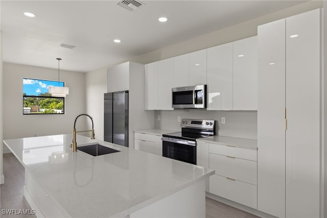 kitchen with decorative light fixtures, light hardwood / wood-style floors, a kitchen island with sink, stainless steel appliances, and sink