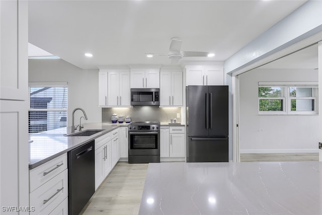 kitchen with a sink, white cabinets, light wood-type flooring, backsplash, and black appliances