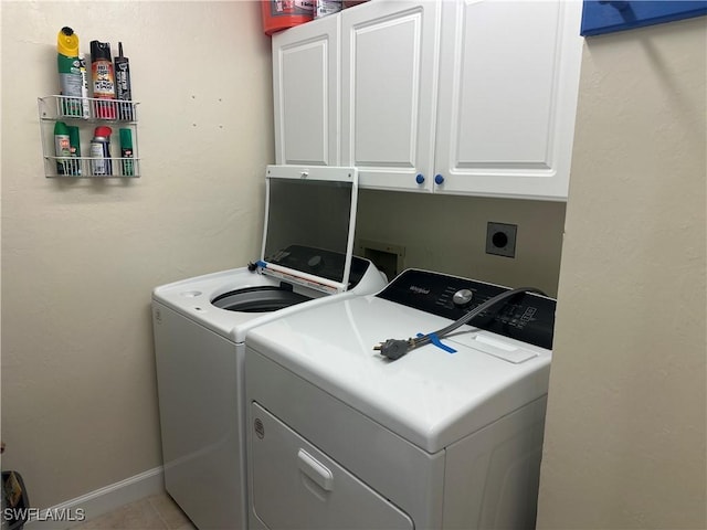 laundry area featuring light tile patterned flooring, washing machine and dryer, cabinet space, and baseboards