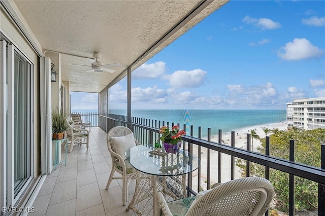 balcony with a water view, a beach view, and ceiling fan