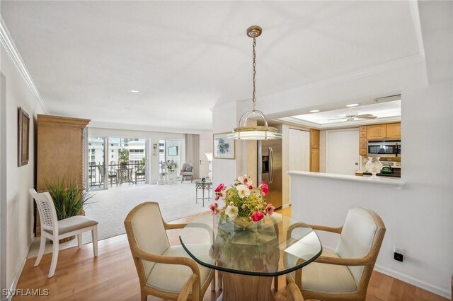 dining space featuring a tray ceiling, baseboards, crown molding, and light wood finished floors