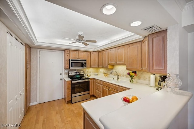 kitchen featuring stainless steel appliances, sink, light wood-type flooring, and a tray ceiling