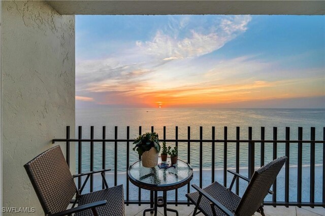 balcony at dusk featuring a water view