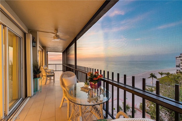 balcony at dusk featuring a water view, a ceiling fan, and a view of the beach