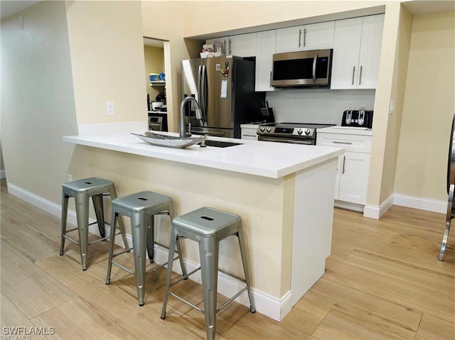 kitchen with light wood-type flooring, appliances with stainless steel finishes, white cabinetry, kitchen peninsula, and a kitchen bar