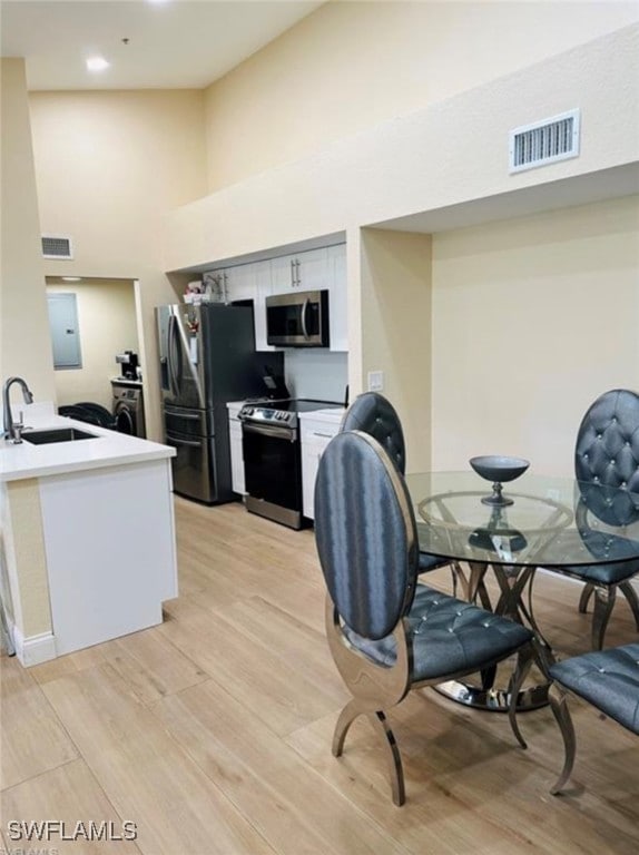 kitchen with appliances with stainless steel finishes, light hardwood / wood-style floors, white cabinetry, sink, and a towering ceiling