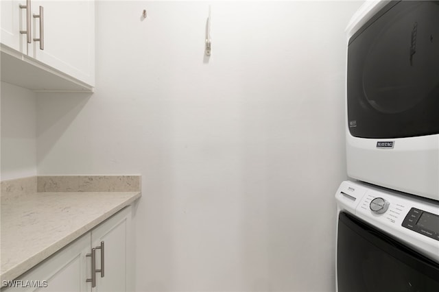 laundry room featuring cabinets and stacked washer / dryer