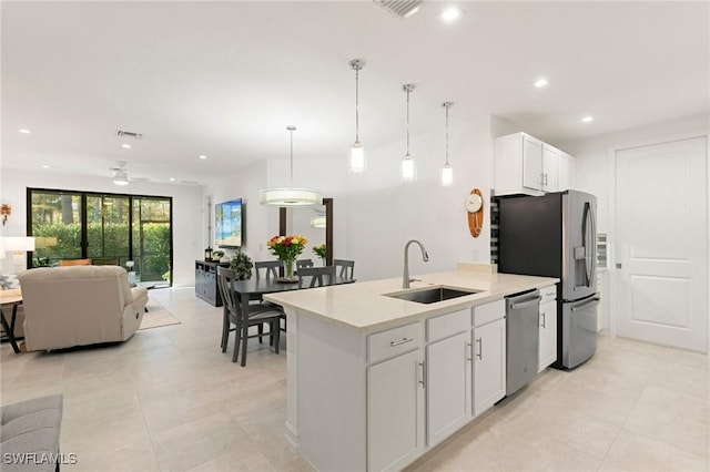 kitchen with appliances with stainless steel finishes, pendant lighting, sink, white cabinets, and a kitchen island with sink