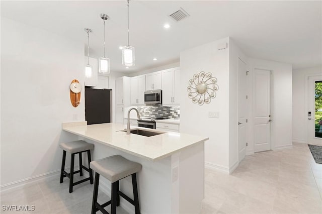 kitchen with pendant lighting, sink, appliances with stainless steel finishes, tasteful backsplash, and white cabinets