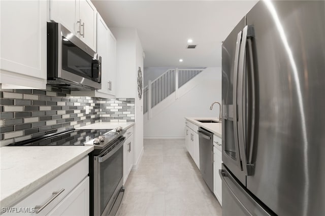 kitchen featuring light tile patterned flooring, sink, light stone counters, stainless steel appliances, and white cabinets