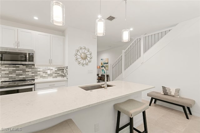 kitchen with sink, a breakfast bar area, appliances with stainless steel finishes, backsplash, and decorative light fixtures