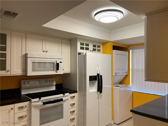 kitchen with stacked washer / dryer, white appliances, a tray ceiling, white cabinets, and ornamental molding