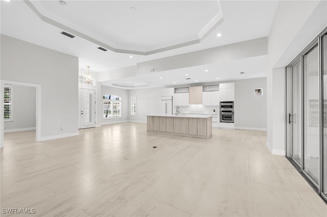 unfurnished living room featuring an inviting chandelier, sink, a towering ceiling, crown molding, and a raised ceiling