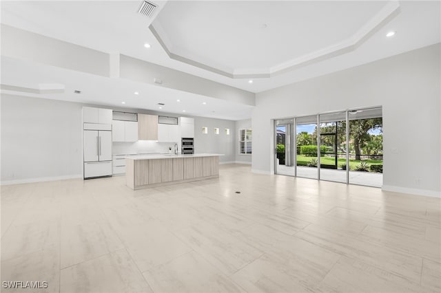 unfurnished living room featuring a raised ceiling, sink, and a towering ceiling