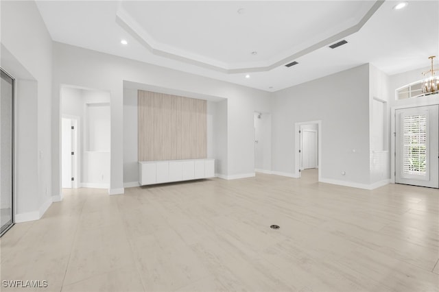 unfurnished living room with a tray ceiling, light wood-type flooring, and a notable chandelier