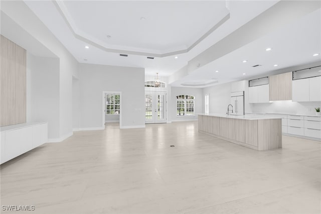 unfurnished living room with sink, ornamental molding, a notable chandelier, and a raised ceiling