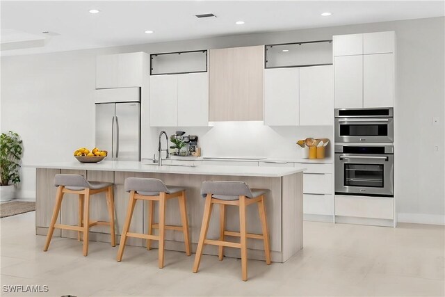 kitchen featuring stainless steel appliances, white cabinetry, sink, and a center island with sink