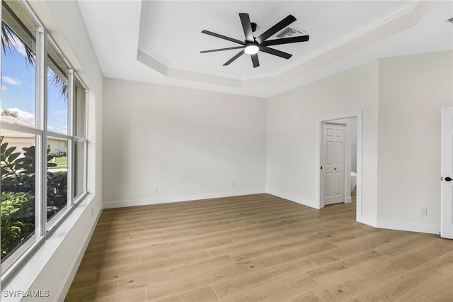 unfurnished room with crown molding, a tray ceiling, and light wood-type flooring