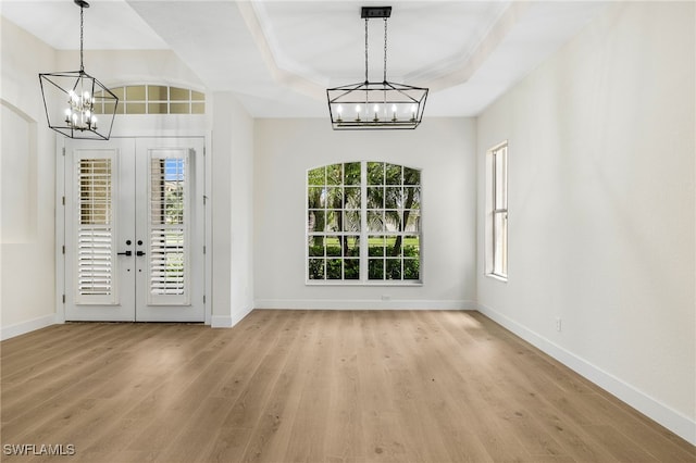 entryway with an inviting chandelier, french doors, a raised ceiling, and light wood-type flooring