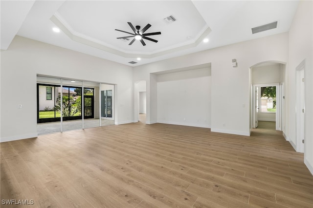 unfurnished living room featuring crown molding, a tray ceiling, ceiling fan, and light wood-type flooring