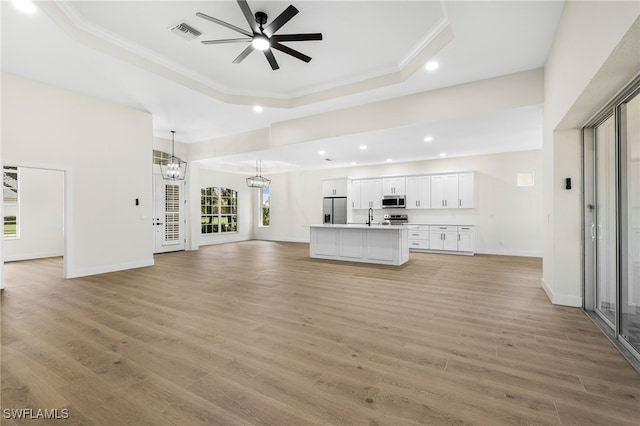 unfurnished living room featuring ornamental molding, ceiling fan with notable chandelier, light hardwood / wood-style flooring, and a tray ceiling