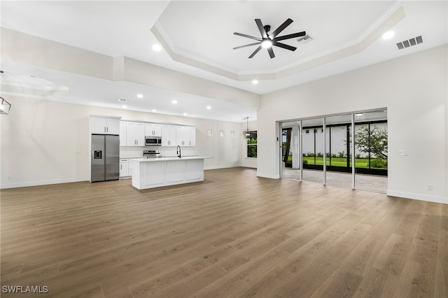 unfurnished living room with ceiling fan, a tray ceiling, sink, and light hardwood / wood-style flooring