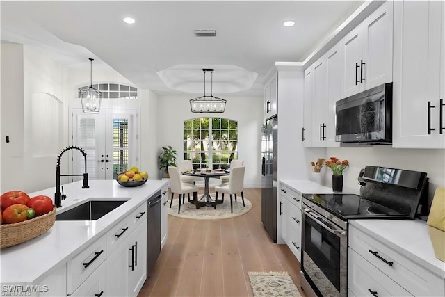 kitchen featuring sink, white cabinetry, a raised ceiling, stainless steel appliances, and light hardwood / wood-style floors