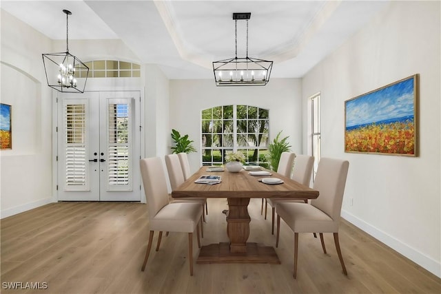 dining room featuring hardwood / wood-style flooring, a healthy amount of sunlight, a tray ceiling, and a chandelier