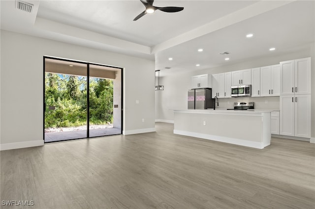 kitchen featuring an island with sink, stainless steel appliances, white cabinetry, ceiling fan, and light wood-type flooring