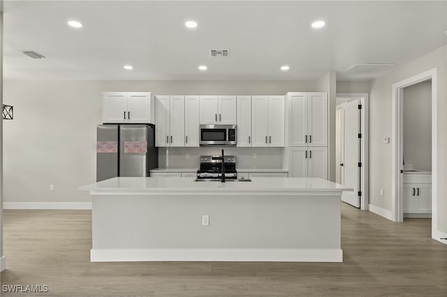 kitchen with a center island with sink, stainless steel appliances, light wood-type flooring, and white cabinets