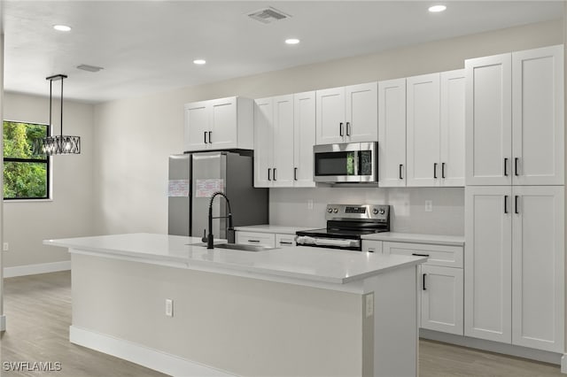 kitchen featuring white cabinetry, decorative light fixtures, stainless steel appliances, sink, and a center island with sink