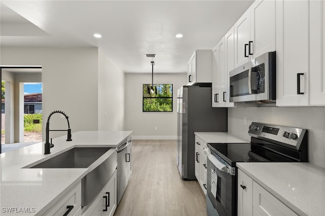 kitchen with light wood-type flooring, white cabinets, appliances with stainless steel finishes, and light stone counters