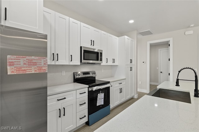 kitchen featuring white cabinets, light wood-type flooring, light stone counters, stainless steel appliances, and sink