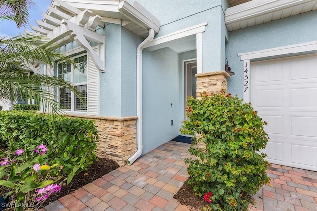 view of exterior entry with a garage, stone siding, and stucco siding