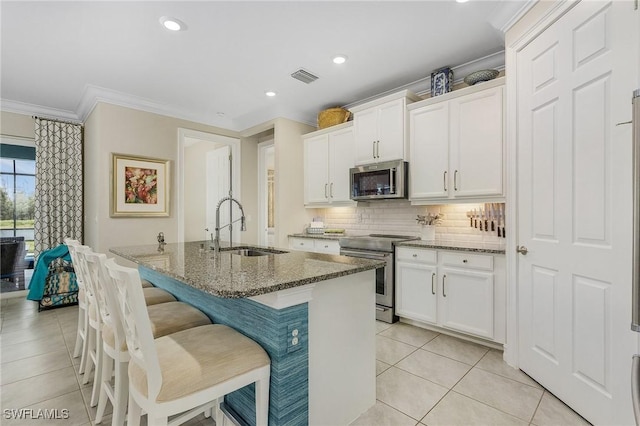 kitchen with white cabinets, a breakfast bar, dark stone countertops, stainless steel appliances, and a sink