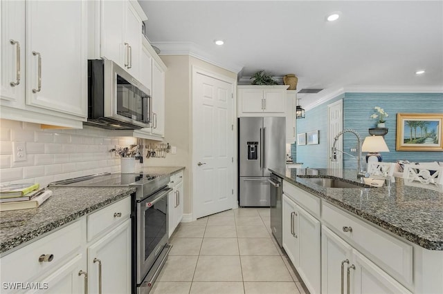 kitchen featuring dark stone counters, premium appliances, crown molding, white cabinetry, and a sink