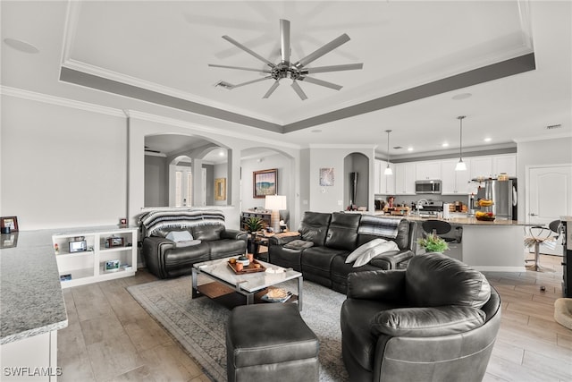 living room featuring a tray ceiling, ceiling fan, crown molding, and light hardwood / wood-style flooring