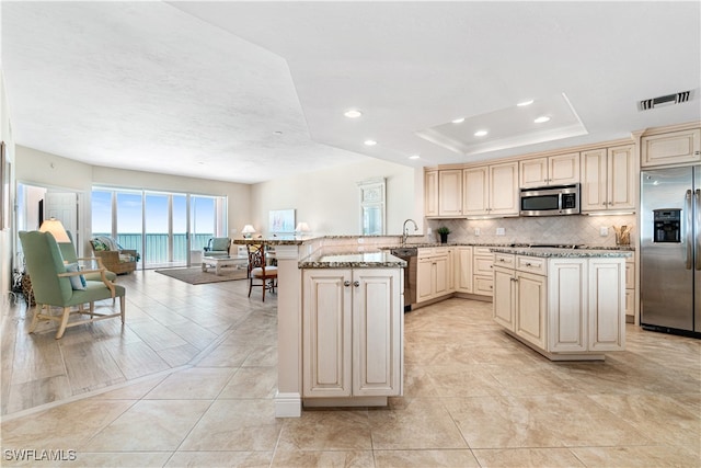 kitchen featuring appliances with stainless steel finishes, cream cabinetry, a raised ceiling, and light stone countertops