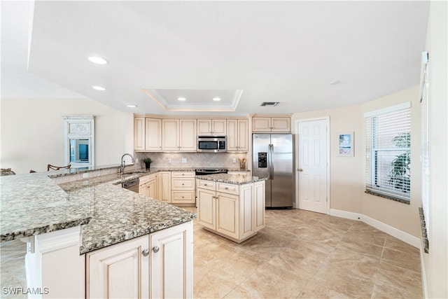 kitchen featuring a raised ceiling, light stone countertops, backsplash, stainless steel appliances, and kitchen peninsula