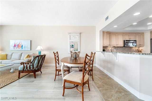 dining area with a tray ceiling, ornamental molding, sink, and light tile patterned flooring