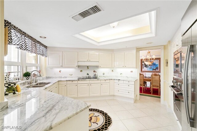 kitchen featuring light tile patterned flooring, light stone counters, a tray ceiling, sink, and a chandelier