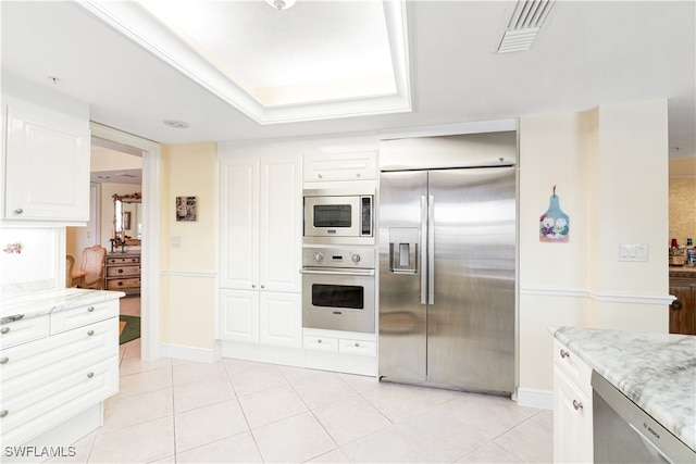 kitchen with light stone countertops, light tile patterned flooring, white cabinetry, and built in appliances