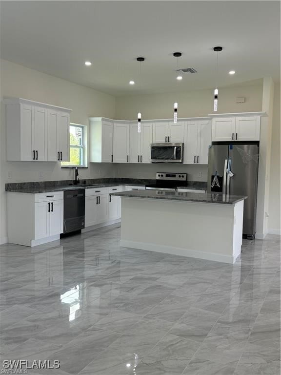 kitchen featuring appliances with stainless steel finishes, white cabinets, a kitchen island, and decorative light fixtures