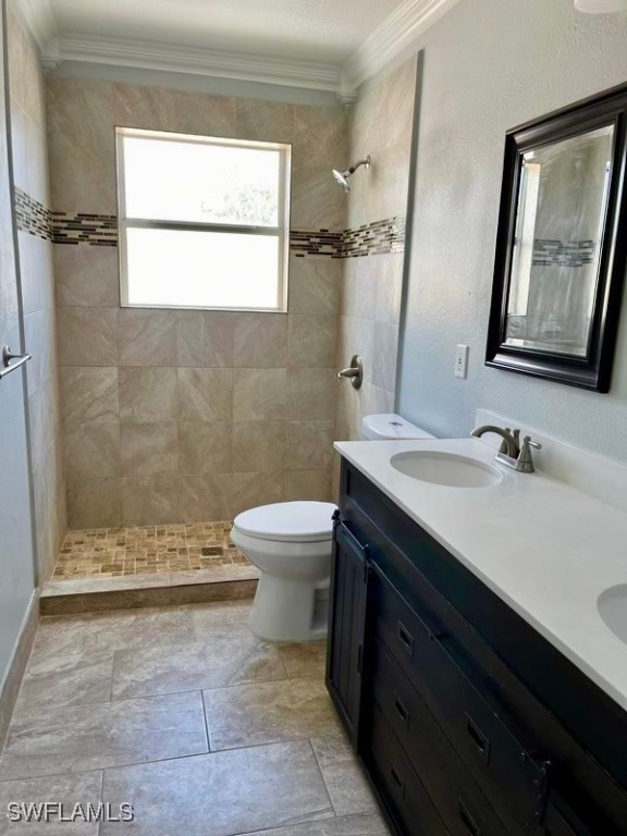 bathroom with toilet, a tile shower, ornamental molding, and vanity