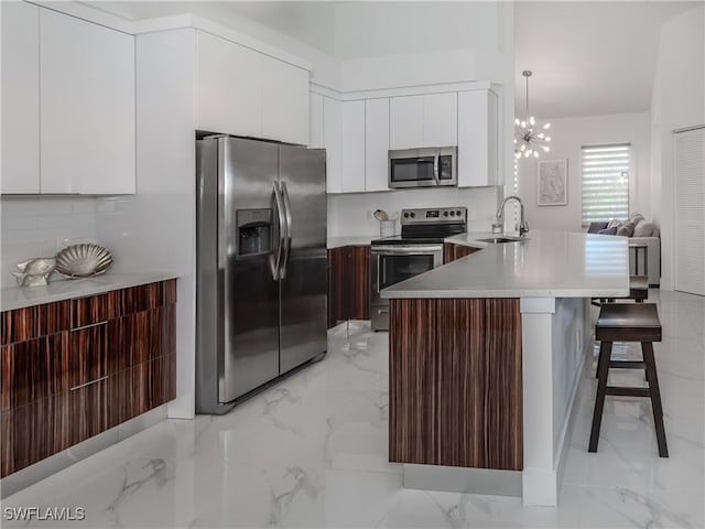 kitchen with hanging light fixtures, appliances with stainless steel finishes, a notable chandelier, kitchen peninsula, and a kitchen breakfast bar