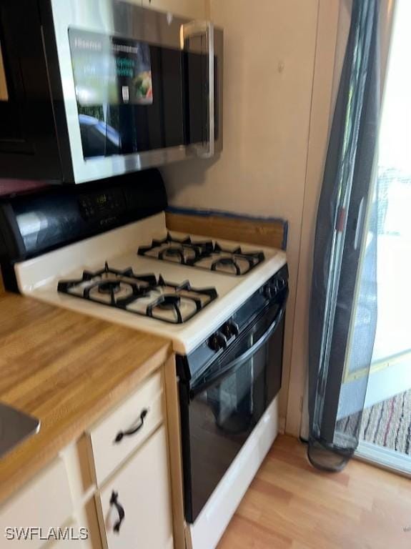 52 Heath Aster Ln, Lehigh Acres, FL 33936 - kitchen with range with gas stovetop, stainless steel microwave, light wood-style floors, and white cabinets