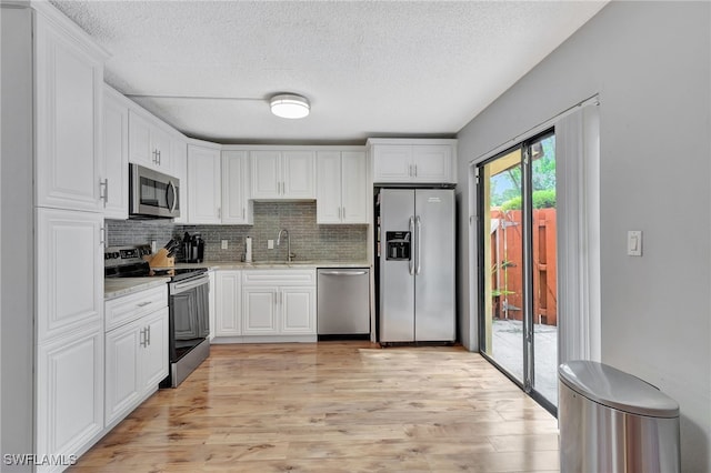 kitchen with light stone countertops, light hardwood / wood-style floors, stainless steel appliances, sink, and white cabinetry