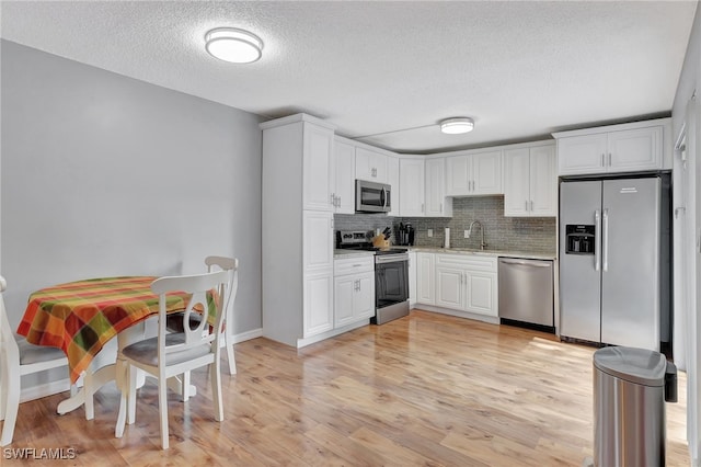 kitchen featuring light wood-type flooring, white cabinetry, tasteful backsplash, stainless steel appliances, and sink